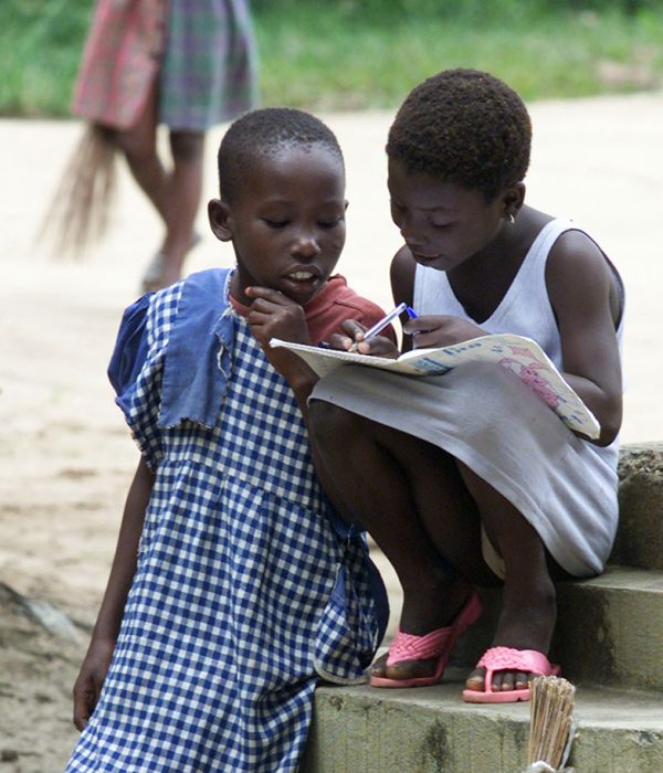 two young girls study together, 19 September 2001 in the public school of N'Zikro village, located about a hundred kilometers West away from Abidjan. Some of them have to walk more than 14 kms to get there. During the first day of the start of the new school year, children clean the school yard and their classroom. Pupils begin to study on the second day only. The installations are very simple : wooden desks, holes in the wall to let the light and the air pass through, and at last a black board against the wall. Some of the kids have to wear a uniform (white and blue for the girls and khaki for the boys). Near 250 pupils attend class in this bush school, divided in six classes from 11th grade to 7th grade.   AFP PHOTO GEORGES GOBET